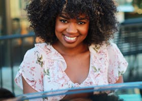 Smiling woman with natural afro hairstyle outdoors in a floral dress, capturing joy on a sunny day.