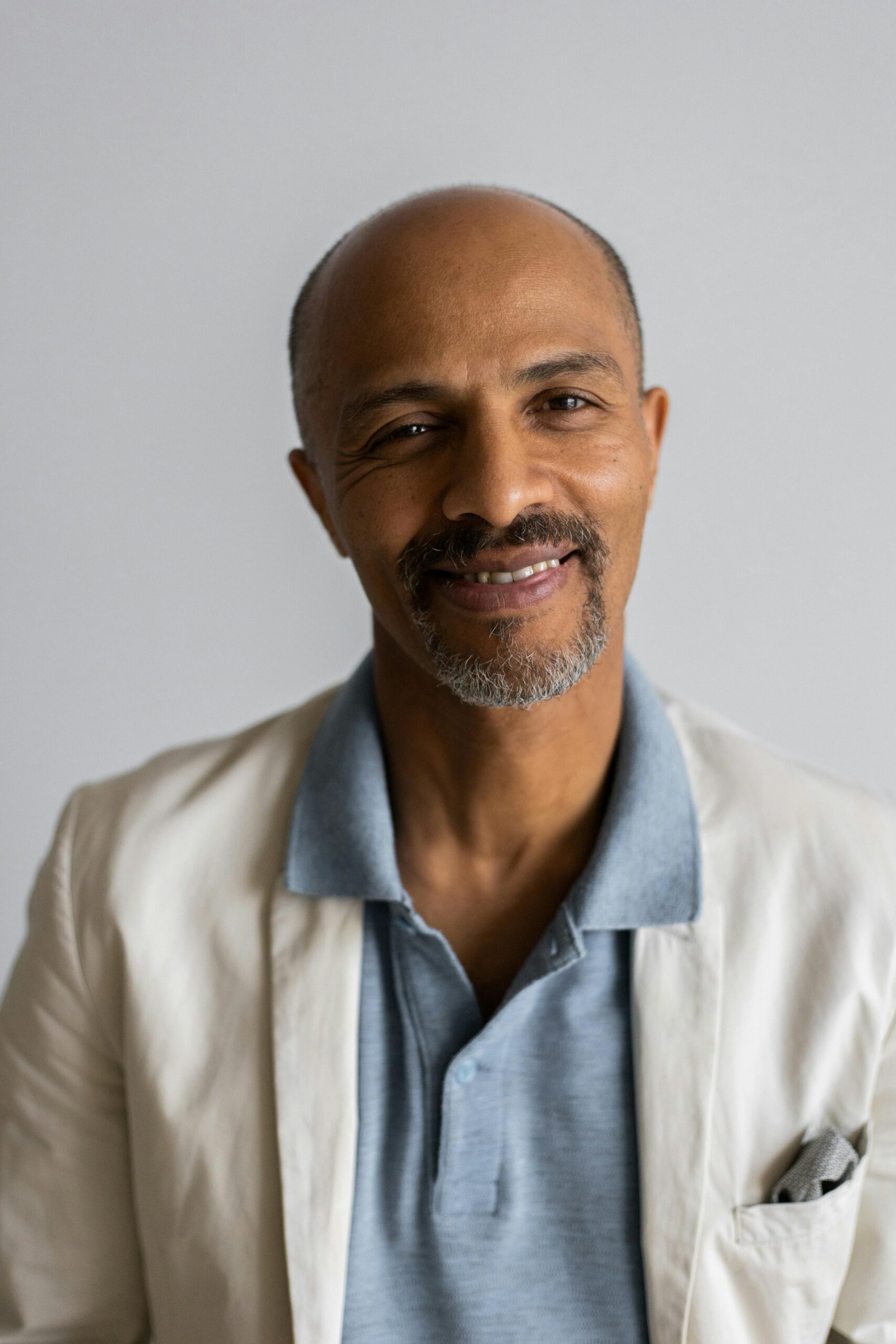 Delighted adult Indian male with beard in jacket and polo shirt on white background looking at camera